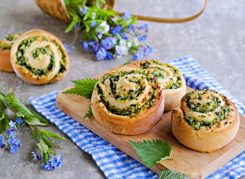 Twisted yeast buns stuffed with nettles, green onions and cheese on a wooden board on a gray concrete background. Recipes with wild herbs.