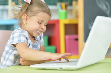 Portrait of curious little girl using laptop at desk