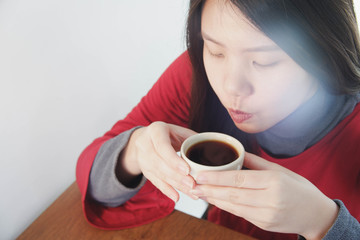 Image of an asian woman sipping a hot cup of coffee with white flare.