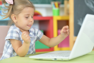 Fototapeta na wymiar Portrait of curious little girl using laptop at desk
