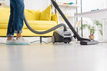 Fototapeta premium Cropped view of woman with vacuum cleaner near coffee table in living room