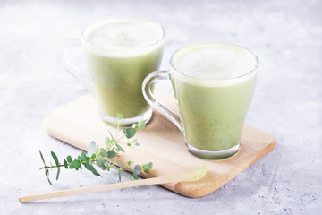 Two glass cups of fresh matcha latte, green tea with milk decorated with eucalyptus on gray background, close up
