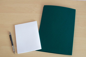 white notebook with dark green folder on the wooden table