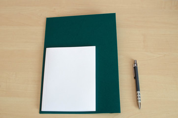 white notebook with dark green folder on the wooden table