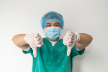 Doctor thumb doing dislike. Doctor in medical clothes shows hand gesture denial. Thumb down. Emotion of negativity. Young asian in a protective mask.