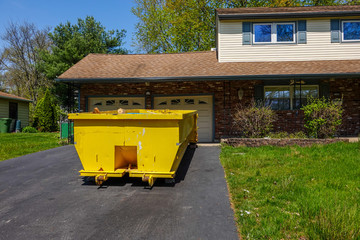A long yellow empty dumpster seen in the driveway in front of a home being renovated
