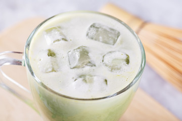 Close up of a pieces of ice in a glass with fresh matcha latte, green tea with milk on a gray background