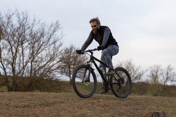 Fototapeta premium Sports brutal bearded guy on a modern mountain bike. Cyclist on the green hills in the spring.