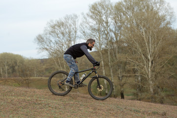 Sports brutal bearded guy on a modern mountain bike. Cyclist on the green hills in the spring.