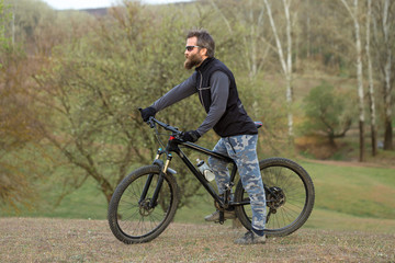 Fototapeta na wymiar Sports brutal bearded guy on a modern mountain bike. Cyclist on the green hills in the spring.