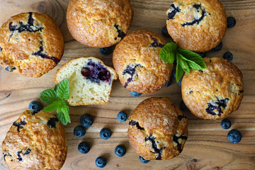 Homemade blueberry muffins on wooden table garnished with fresh blueberries and mint leaf. Top view.