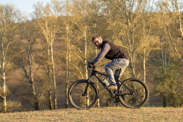 Obraz premium Sports brutal bearded guy on a modern mountain bike. Cyclist on the green hills in the spring.