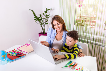 Kind mother helping her son doing homework online. Mother Helping Son With Homework during Covid-19 Coronavirus and Learning from home. Smiling mother helping son with homework on laptop at home