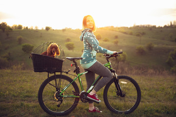 Obraz premium Young woman having fun near countryside park, riding bike, traveling with companion spaniel dog. Calm nature, spring day, positive emotions. Sportive, active leisure activity. Walking together.