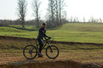 Fototapeta premium Cyclist in shorts and jersey on a modern carbon hardtail bike with an air suspension fork standing on a cliff against the background of fresh green spring forest