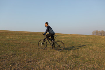 Cyclist in shorts and jersey on a modern carbon hardtail bike with an air suspension fork standing on a cliff against the background of fresh green spring forest