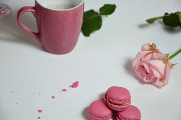 Three pink almond macaroons and mug with coffee on a white wooden background next to a pale pink rose. good morning concept