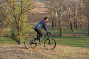 Fototapeta premium Cyclist in shorts and jersey on a modern carbon hardtail bike with an air suspension fork standing on a cliff against the background of fresh green spring forest