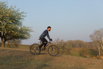 Naklejka premium Cyclist in shorts and jersey on a modern carbon hardtail bike with an air suspension fork standing on a cliff against the background of fresh green spring forest