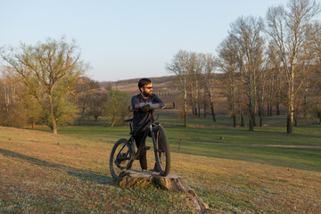 Cyclist in shorts and jersey on a modern carbon hardtail bike with an air suspension fork standing on a cliff against the background of fresh green spring forest