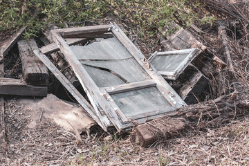 Old window frames with broken glass and thick wooden beams lie on the ground. Glasses are dirty. Around the withered grass. Horizontal.