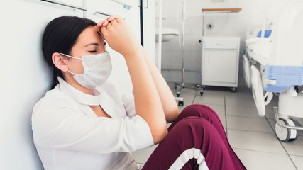 Overworked nurse sitting in hospital hallway. Tired after hard day medical staff in mask. Recession...