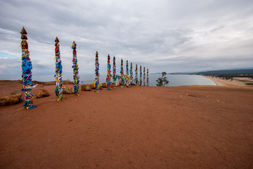 Buddhist sacred pillars with ribbons on the island of Olkhon on Lake Baikal. Many pillars in a row. The sky is cloudy. Horizontal.