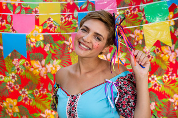 Cheerful Young blonde woman dressed in plaid dress smiling with broad smile at evening typical arraial. Festive June Party, brazilian festival, celebration concept.