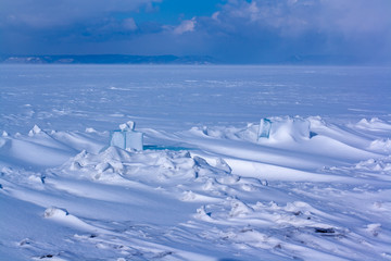 A lake with snow on top of ice and carved pieces of ice. Winter landscape. Mountains in the background of Lake Baikal. Focus on blocks of ice. Horizontal.