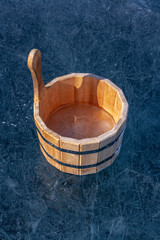 A wooden tub with ice inside is on ice. Ice with bubbles and cracks. Iron tightening rings connect parts of the tub. Sunny. Vertical.