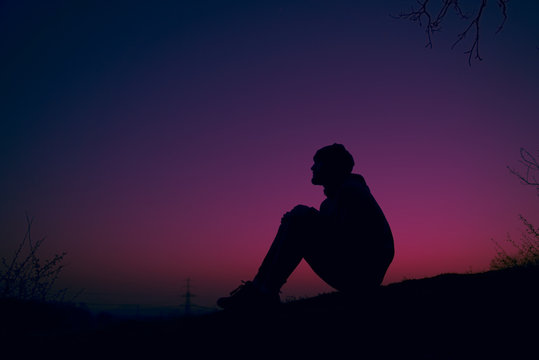 Silhouette of man sitting on swinging hill dreaming at sunset