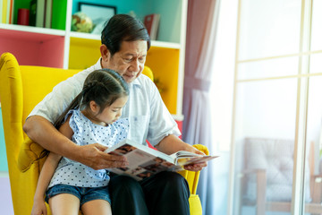 Grandfather read a book with niece at home in weekend, family relationship with elder man and kids. Children interested in colorful pictures, older feeling happiness when stay together with child  .