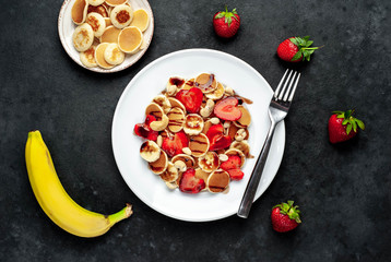 Mini pancakes with strawberries, bananas, nuts in a plate on a stone background. delicious breakfast concept
