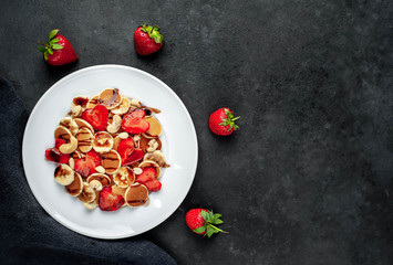 Mini pancakes with strawberries, bananas, nuts in a plate on a stone background. tasty breakfast concept with copy space for your text
