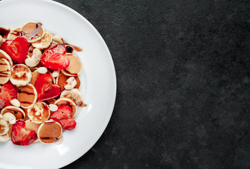 Mini pancakes with strawberries, bananas, nuts in a plate on a stone background. tasty breakfast concept with copy space for your text