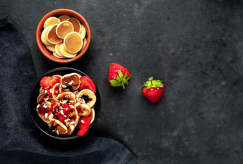 Mini pancakes with strawberries, bananas, nuts in a plate on a stone background. tasty breakfast concept with copy space for your text