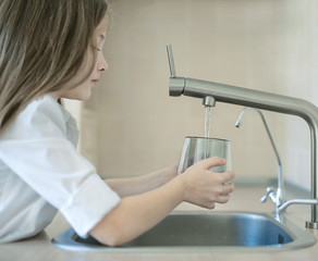 Child is holding a transparent glass. Filling cup beverage. Pouring fresh drink. Consumption of tap...