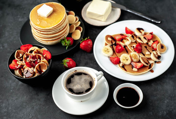 The concept of a delicious breakfast. Coffee and mini pancakes with strawberries, bananas, nuts in a plate and American pancakes in a plate on a stone background 