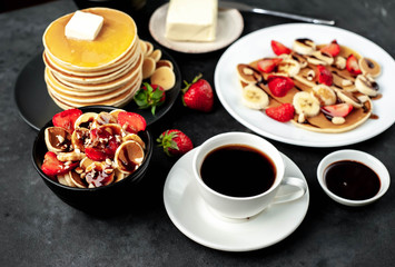 The concept of a delicious breakfast. Coffee and mini pancakes with strawberries, bananas, nuts in a plate and American pancakes in a plate on a stone background 