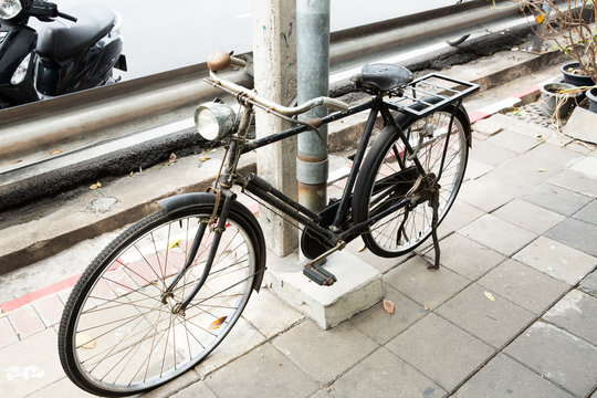Black antique bicycle parked on a foot bath beside an electric pole
