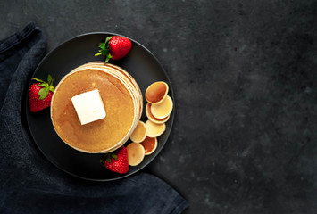 Stack of pancakes with strawberries in a plate on a stone background with copy space for your text