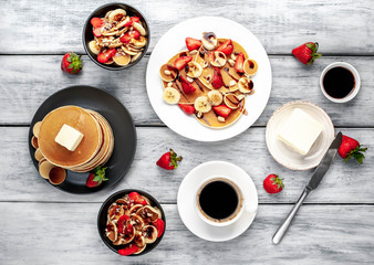 The concept of a delicious breakfast. Coffee and mini pancakes with strawberries, bananas, nuts in a plate and American pancakes in a plate on a wooden background