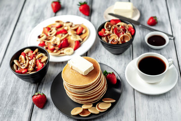The concept of a delicious breakfast. Coffee and mini pancakes with strawberries, bananas, nuts in a plate and American pancakes in a plate on a wooden background