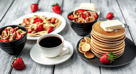 The concept of a delicious breakfast. Coffee and mini pancakes with strawberries, bananas, nuts in a plate and American pancakes in a plate on a wooden background