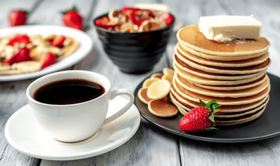 The concept of a delicious breakfast. Coffee and mini pancakes with strawberries, bananas, nuts in a plate and American pancakes in a plate on a wooden background