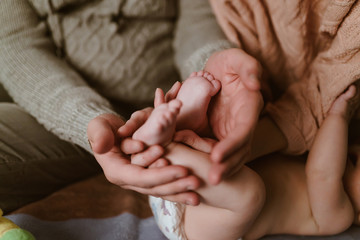 the palms of the father and mother gently hug the small feet of the lying baby, his arms touch the elbow of mom