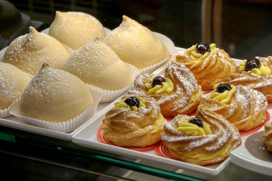 Zeppole and tette delle monache for breakfast in a shop window of an Italian bar