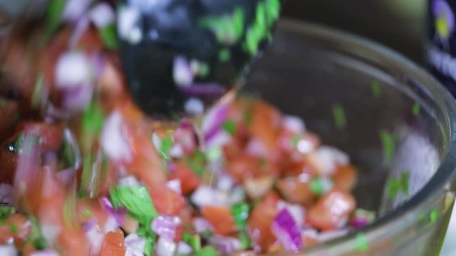 close up view of pico de gallo being mixed in  a bowl. the organic fresh vegetable ingredients are being prepared for a healthy diner and tasty treat that leads for a good lifestyle.