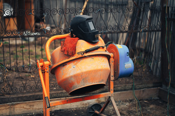 Orange concrete mixer at the construction site, foundation tools