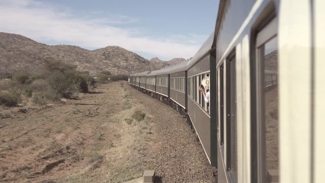Woman photographing mountains while leaning from window during rail journey against sky - Swakopmund, Namibia